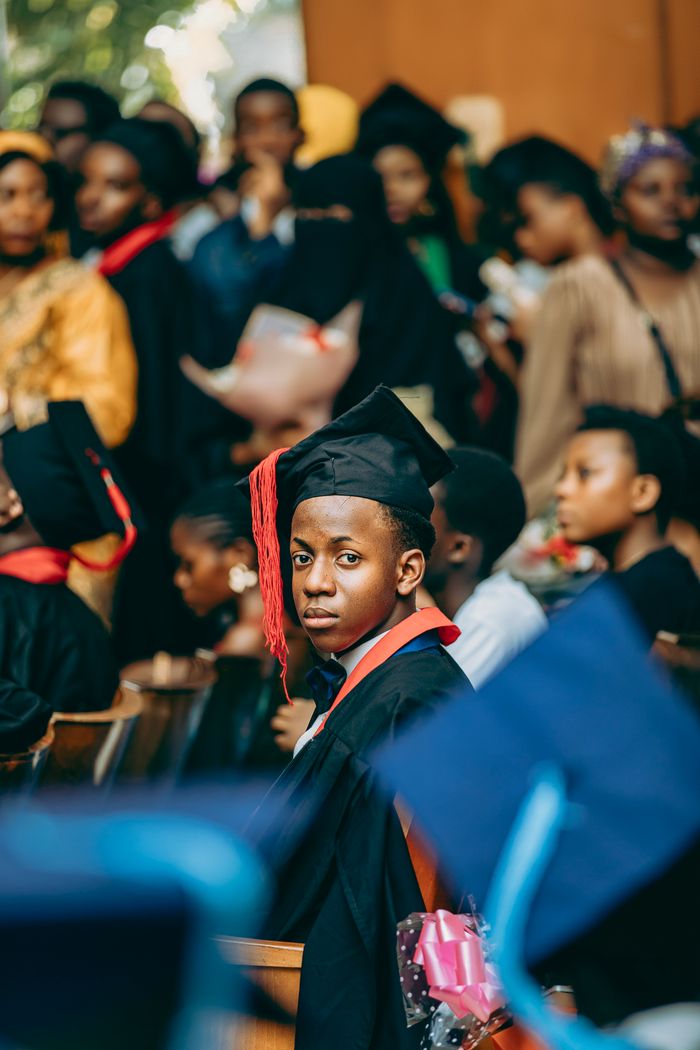 A young graduate wearing a cap and gown amid a crowd at a graduation ceremony.