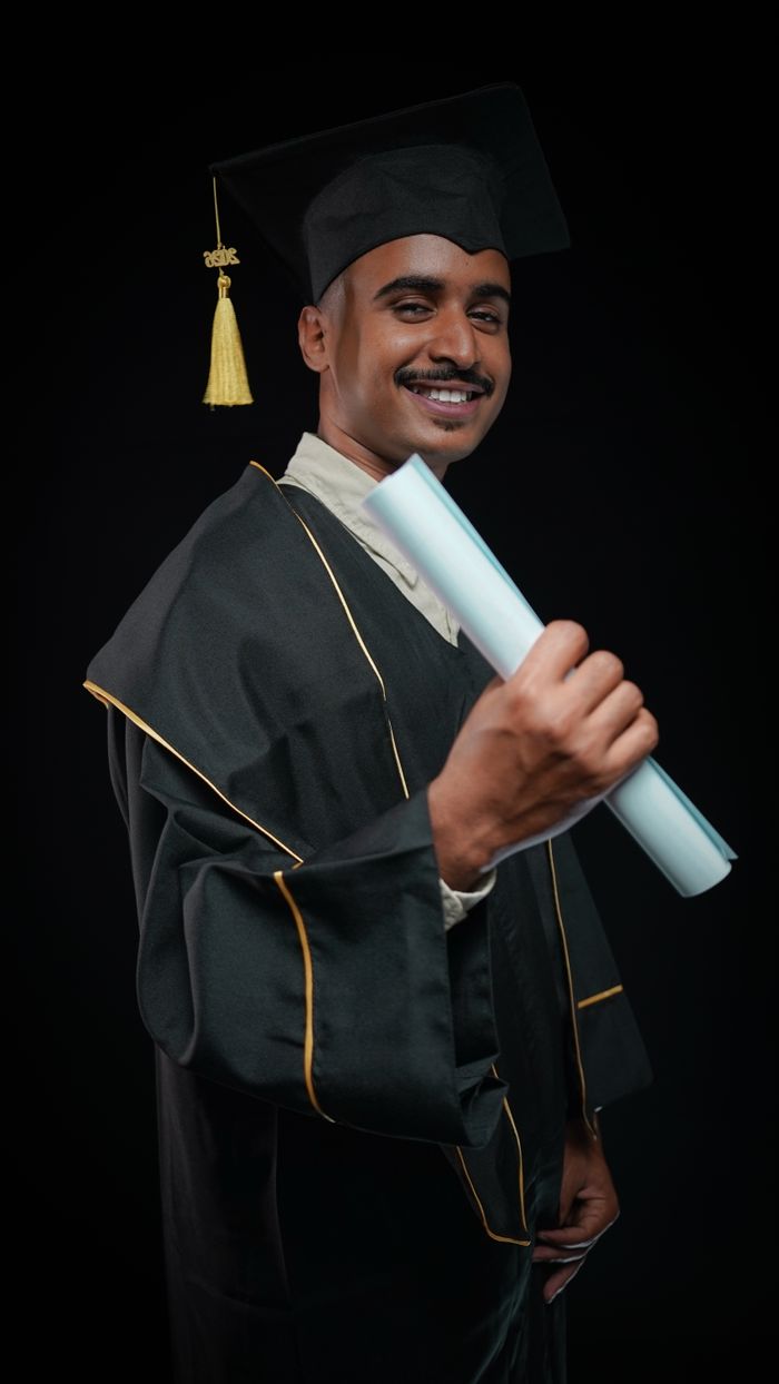 A proud graduate in cap and gown holding a diploma with a smile.